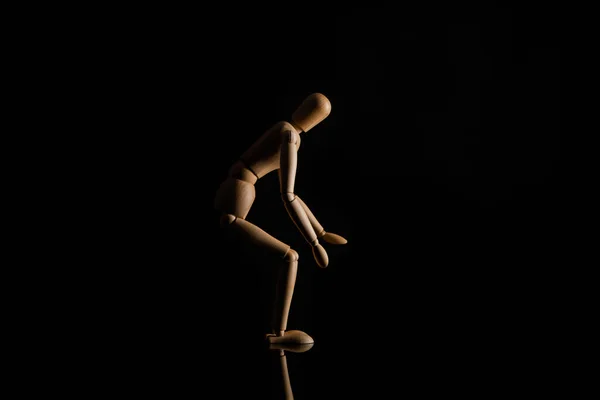 Poupée en bois en position assise sur fond noir — Photo de stock