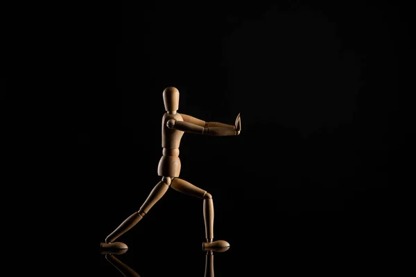 Wooden doll imitating doing lunges on black background — Stock Photo