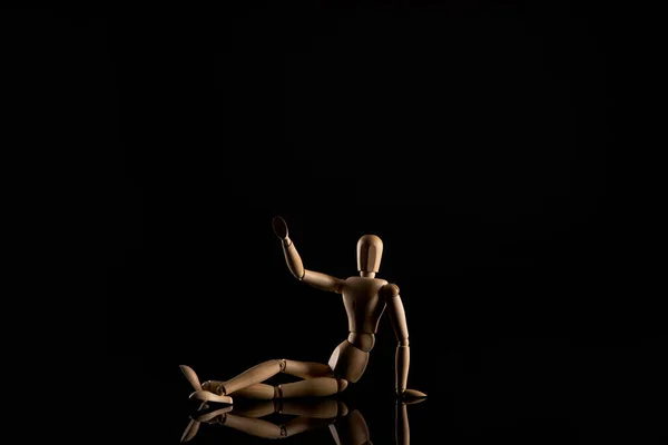 Holzpuppe in Sitzposition mit ausgestreckter Hand und gekreuzten Beinen auf schwarzem Hintergrund — Stockfoto