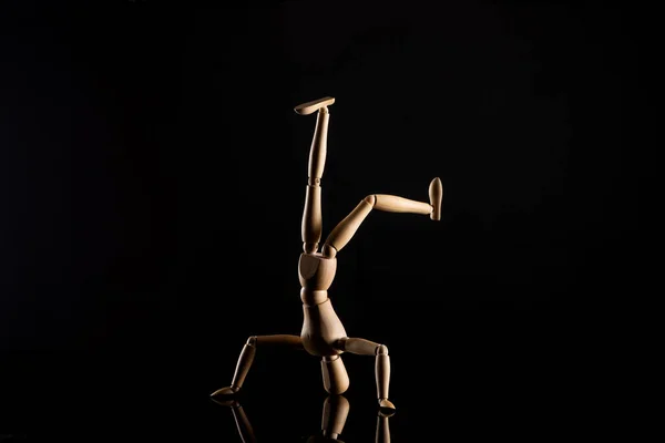 Wooden doll in headstand position on black background — Stock Photo