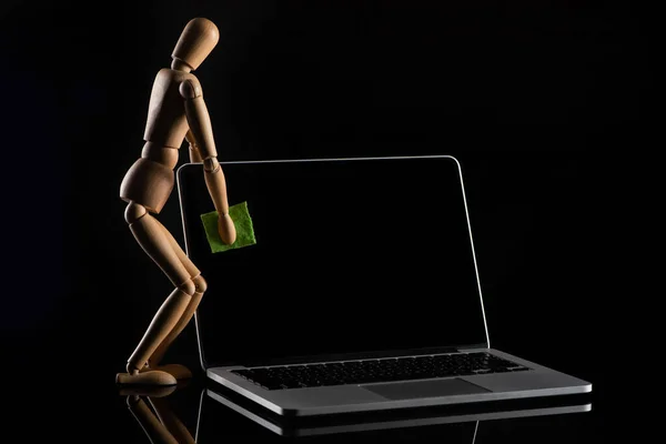 Wooden doll imitating dusting laptop on black — Stock Photo