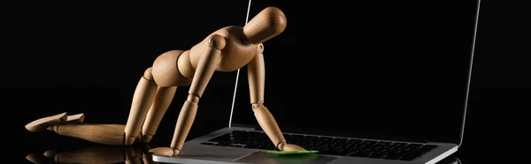Wooden doll on all four position imitating dusting laptop on black background, panoramic shot — Stock Photo