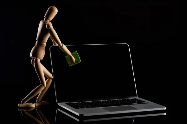 Wooden puppet imitating dusting laptop on black background — Stock Photo