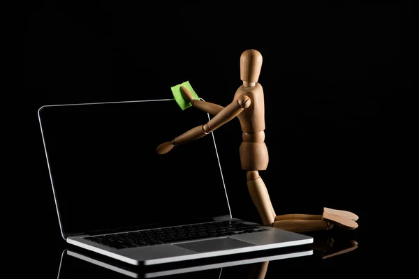 Wooden doll on knees position imitating dusting laptop on black — Stock Photo