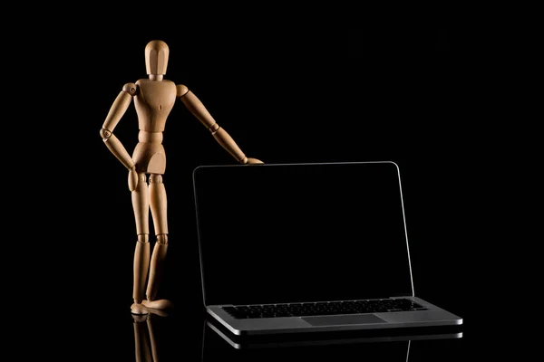 Wooden doll in standing position with hand on hip near laptop on black — Stock Photo