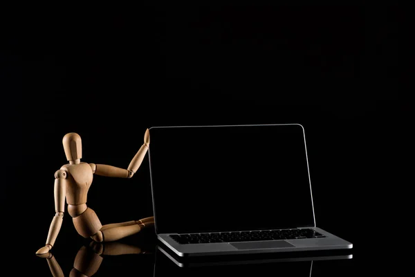 Poupée en bois en position assise près de l'ordinateur portable sur noir — Photo de stock