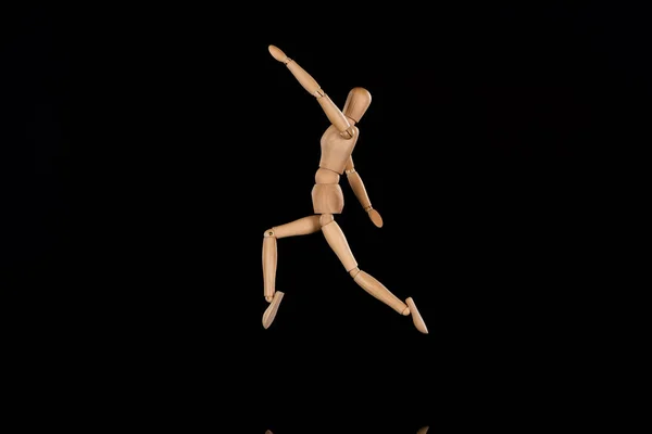 Wooden puppet imitating jumping on black background — Stock Photo