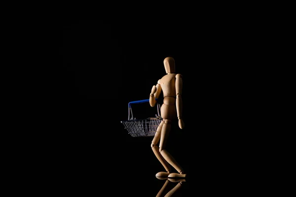 Wooden doll in standing position with shopping basket on black background — Stock Photo