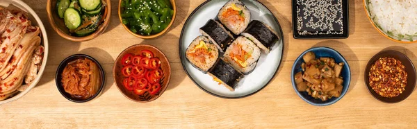 Panoramic shot of bowls with korean side dishes near gimbap on plate — Stock Photo