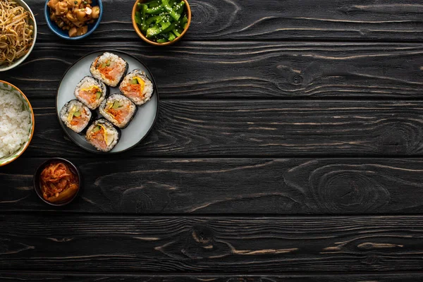 Vue de dessus des bols avec des plats d'accompagnement coréens près de gimbap sur la surface en bois — Photo de stock