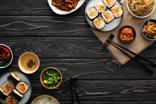 Vista superior de saborosos pratos laterais coreanos perto de gimbap e pauzinhos na superfície de madeira — Fotografia de Stock