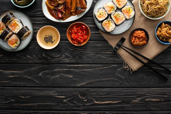 Vue de dessus des plats frais d'accompagnement coréen près de gimbap et baguettes sur la surface en bois — Photo de stock