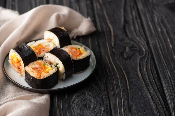 Selektiver Fokus schmackhafter Reisrollen mit Gemüse und Lachs in der Nähe von Baumwollservietten auf Holzoberfläche — Stockfoto