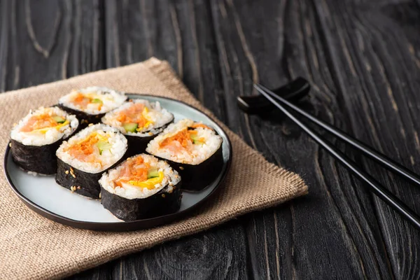 Selektiver Fokus von leckerem Gimbap mit Gemüse und Lachs in der Nähe von Essstäbchen auf Holzoberfläche — Stockfoto