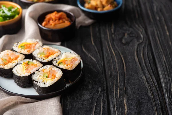 Selektiver Fokus schmackhafter Reisbrötchen in der Nähe koreanischer Beilagen und Baumwollserviette auf Holzoberfläche — Stockfoto