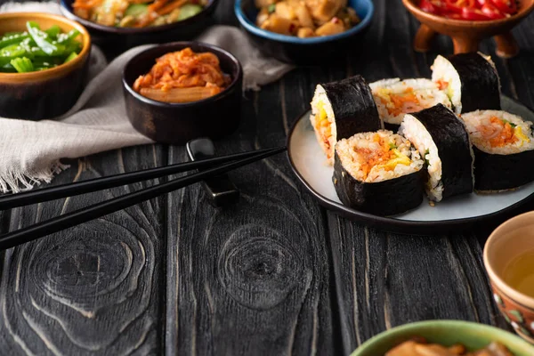 Foco selectivo de delicioso gimbap cerca de platos secundarios coreanos y servilleta de algodón en la superficie de madera - foto de stock