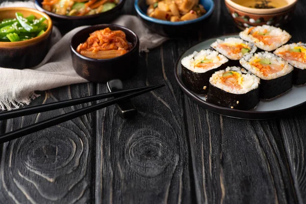 Foyer sélectif de rouleaux de riz coréen près des plats d'accompagnement, baguettes et serviette de coton sur la surface en bois — Photo de stock