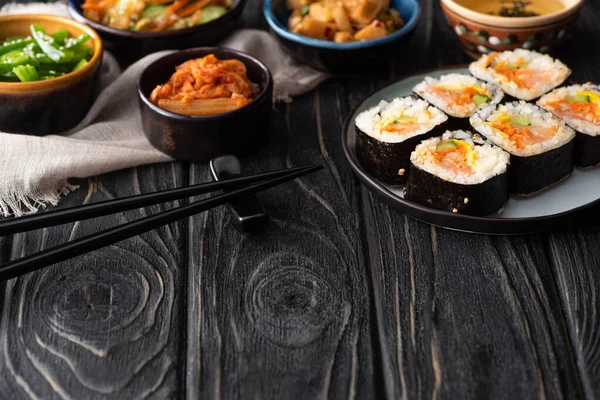 Foco selectivo de rollos de arroz coreano cerca de guarniciones, palillos y servilleta de algodón en la superficie de madera - foto de stock