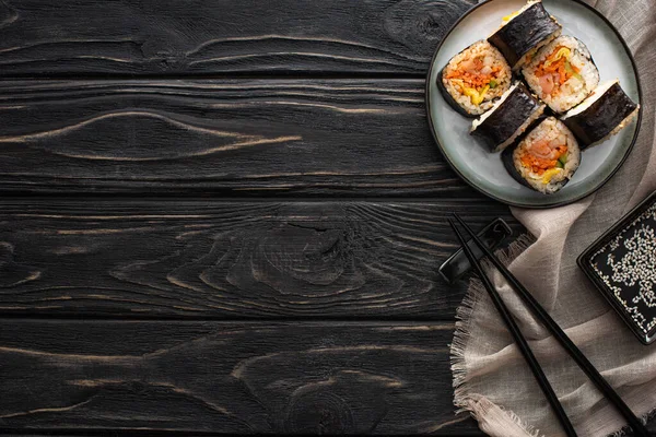 Vista superior de palillos y aceite de sésamo cerca de la placa con gimbap en la superficie de madera - foto de stock