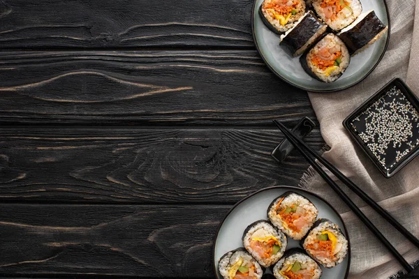 Vista superior de palillos y aceite de sésamo cerca de placas con gimbap en la superficie de madera - foto de stock