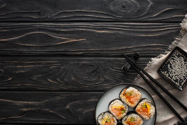 Top view of chopsticks and sesame oil near plate with tasty rice rolls on wooden surface — Stock Photo