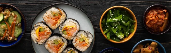 Panoramic shot of korean gimbap near side dishes on wooden surface — Stock Photo