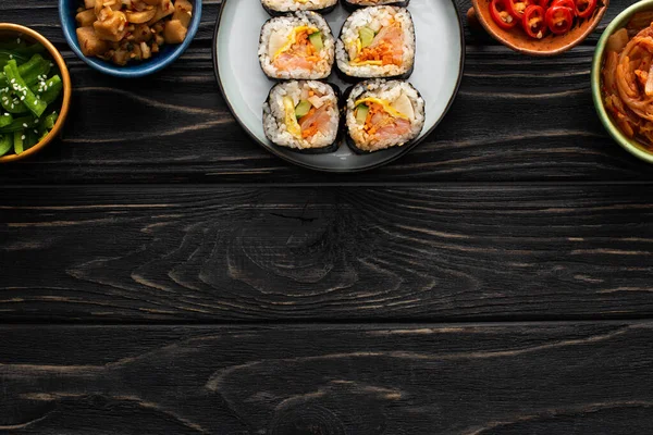 Top view of plate with tasty gimbap near side dishes in bowls on wooden surface — Stock Photo