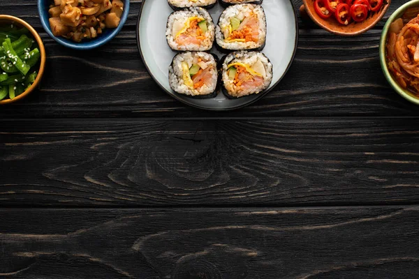 Vue de dessus de la plaque avec un gimbap savoureux près des plats d'accompagnement dans des bols sur la surface en bois — Photo de stock