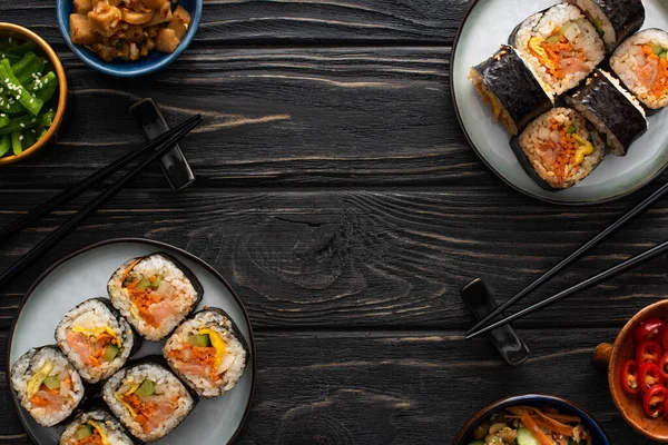 Vue de dessus des baguettes près des assiettes avec de savoureux gimbap et des plats d'accompagnement coréens sur la surface en bois — Photo de stock