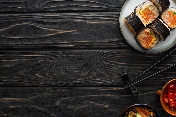 Vue de dessus des baguettes près de la plaque avec gimbap coréen et plats d'accompagnement savoureux sur la surface en bois — Photo de stock