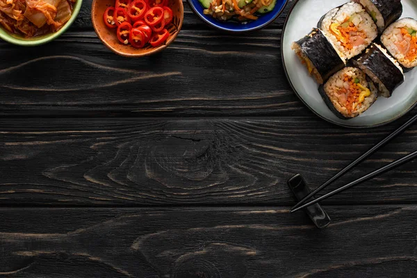 Vue de dessus de la plaque avec gimbap coréen et plats d'accompagnement savoureux près de baguettes sur la surface en bois — Photo de stock