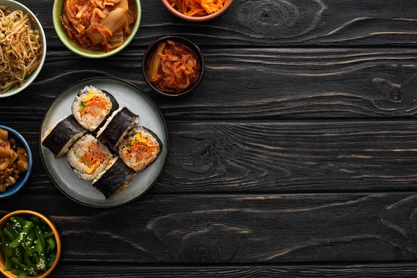 Vista superior da placa com gimbap perto de pratos laterais coreanos saborosos na superfície de madeira — Fotografia de Stock