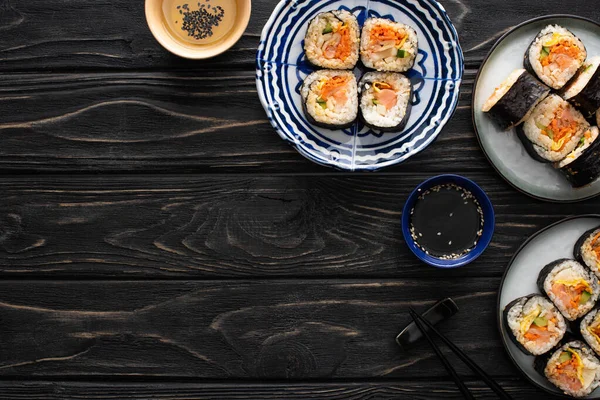 Vista dall'alto di olio di sesamo vicino piatti con gimbap vicino bacchette su superficie di legno — Foto stock