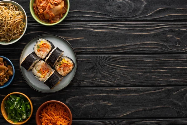 Top view of plate with fresh gimbap near korean side dishes on wooden surface — Stock Photo
