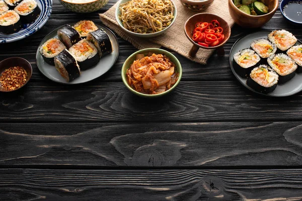 Teller mit frischem Gimbap in der Nähe koreanischer Beilagen auf hölzerner Oberfläche — Stockfoto