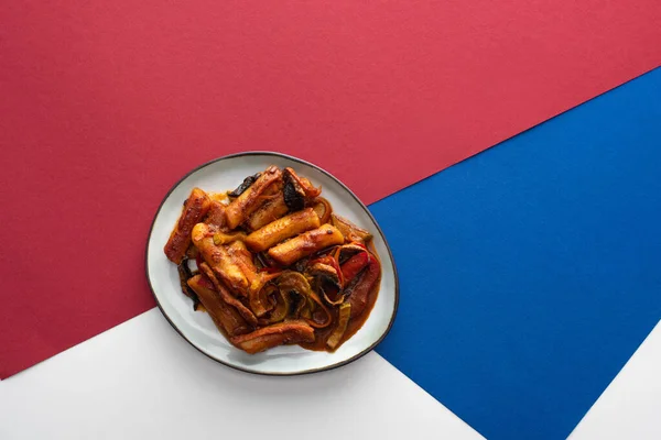 Vista dall'alto di gustoso tteokbokki coreano mescolato fritto su bianco blu e cremisi — Foto stock