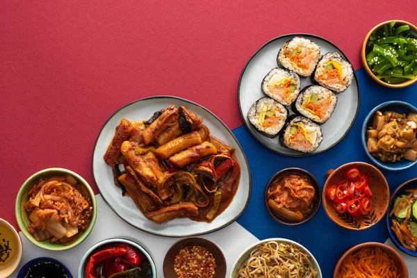 Vue de dessus de gimbap frais près des plats d'accompagnement coréens sur blanc, bleu et cramoisi — Photo de stock