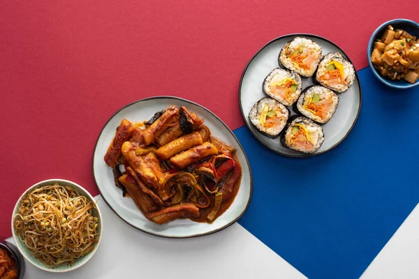 Vista superior de tteokbokki fresco e gimbap perto de pratos laterais coreanos em branco, azul e carmesim — Fotografia de Stock