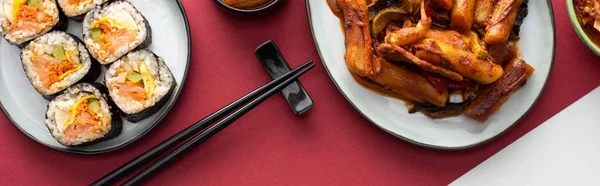 Panoramic shot of fresh tteokbokki and korean gimbap on white and crimson — Stock Photo