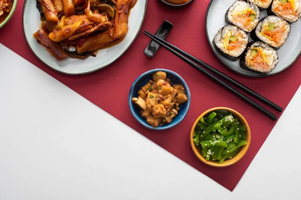 Vue de dessus de tteokbokki frais, gimbap coréen et plats d'accompagnement sur blanc et cramoisi — Photo de stock