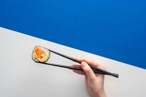 Vista ritagliata di donna che tiene bacchette con gimbap coreano su bianco e blu — Foto stock