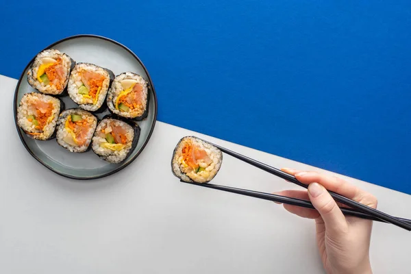 Vue du dessus de la femme tenant des baguettes avec gimbap coréen sur blanc et bleu — Photo de stock