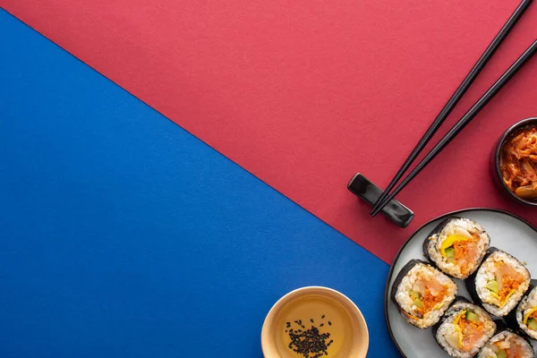 Vista dall'alto del piatto con delizioso gimbap vicino all'olio di sesamo e kimchi su cremisi e blu — Foto stock