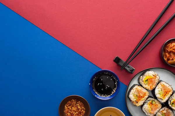 Vue de dessus de sauce soja et huile de sésame près de gimbap sur cramoisi et bleu — Photo de stock