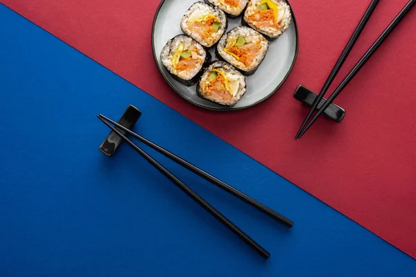 Top view of chopsticks near plate with delicious gimbap on crimson and blue — Stock Photo