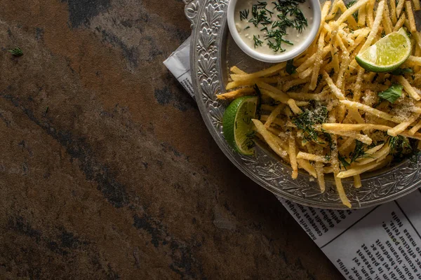 Vista superior de la lima en rodajas cerca de papas fritas y salsa de ajo en la superficie de mármol - foto de stock