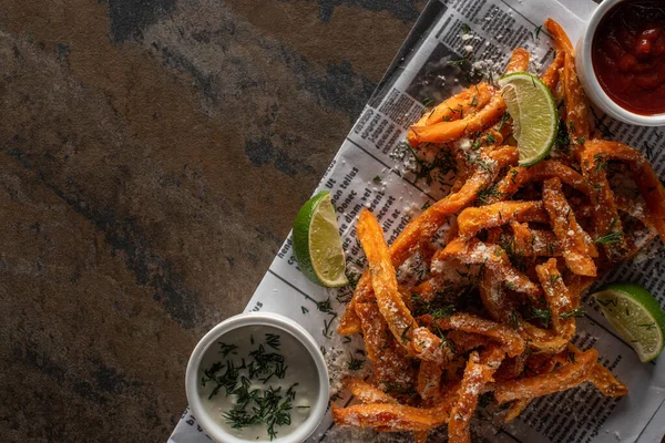 Top view of salty french fries and sliced lime on newspaper and marble surface — Stock Photo