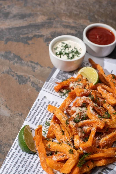 Saborosas batatas fritas, limão fatiado, molho de alho e ketchup no jornal — Fotografia de Stock