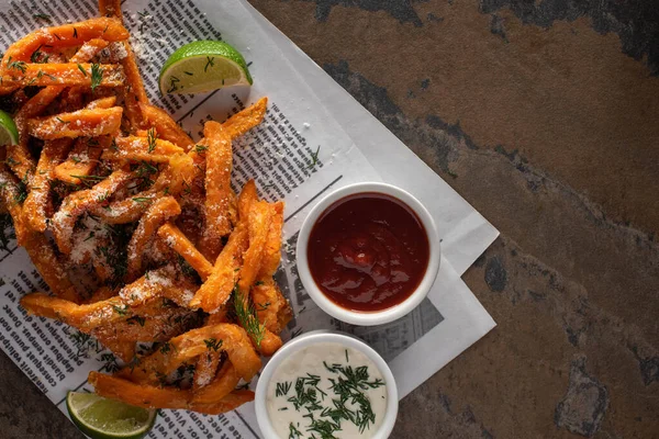 Vista superior de papas fritas saladas, lima en rodajas, salsa de ajo y ketchup en el periódico - foto de stock