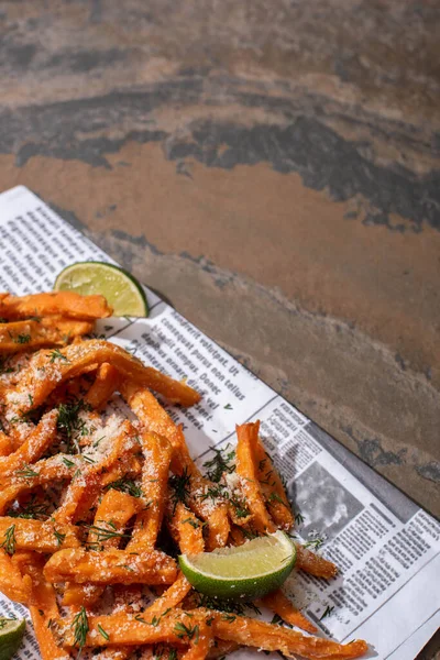 Salty french fries and tasty, sliced lime on newspaper with text and marble surface — Stock Photo
